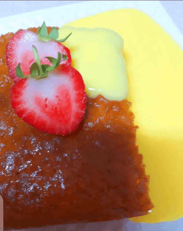 A close-up of a plate containing malva pudding with a strawberry as garnish.