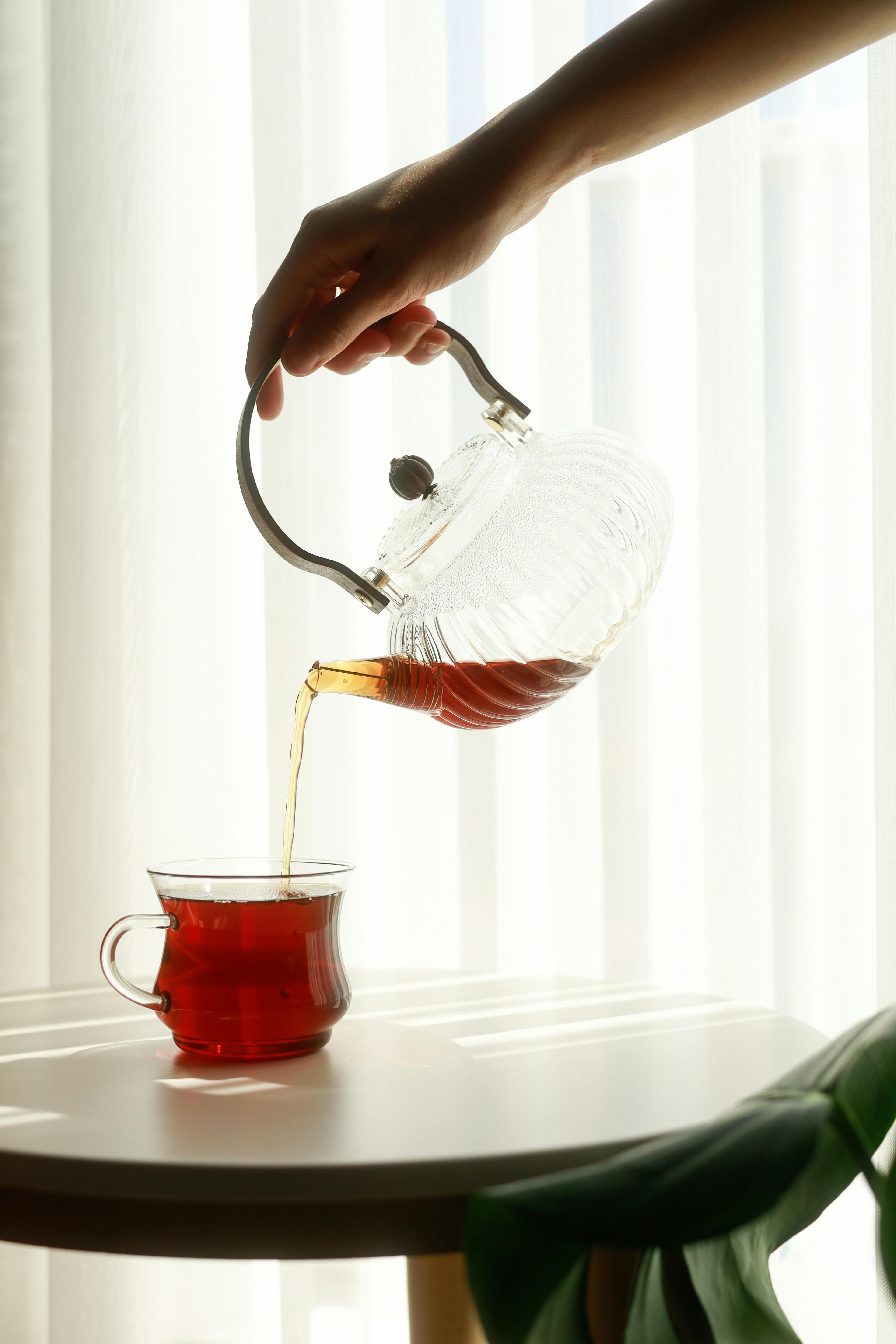 Hot tea being poured from a glass kettle to a glass cup.